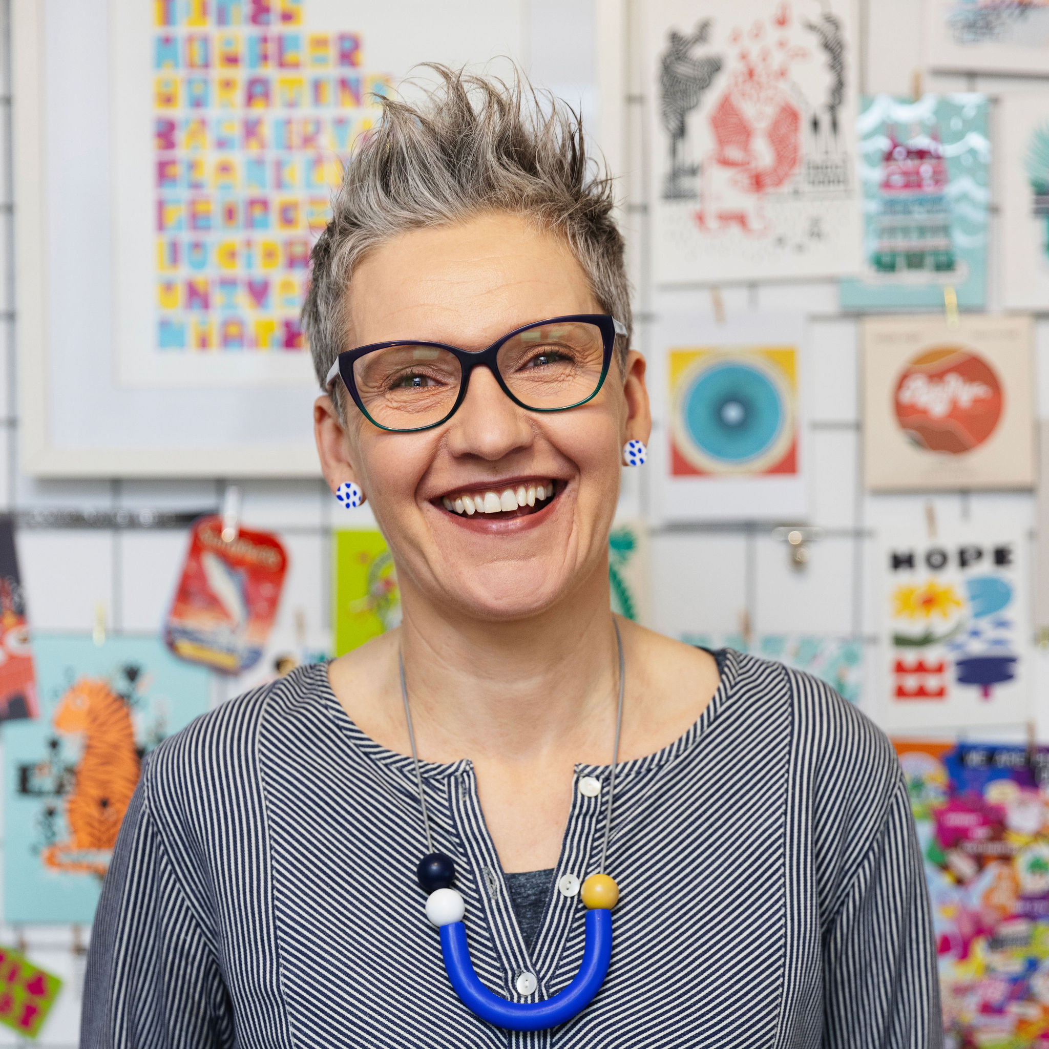 Photo of Bristol based illustrator Carys Tait, standing in front of a notice board with colourful images and illustrations
